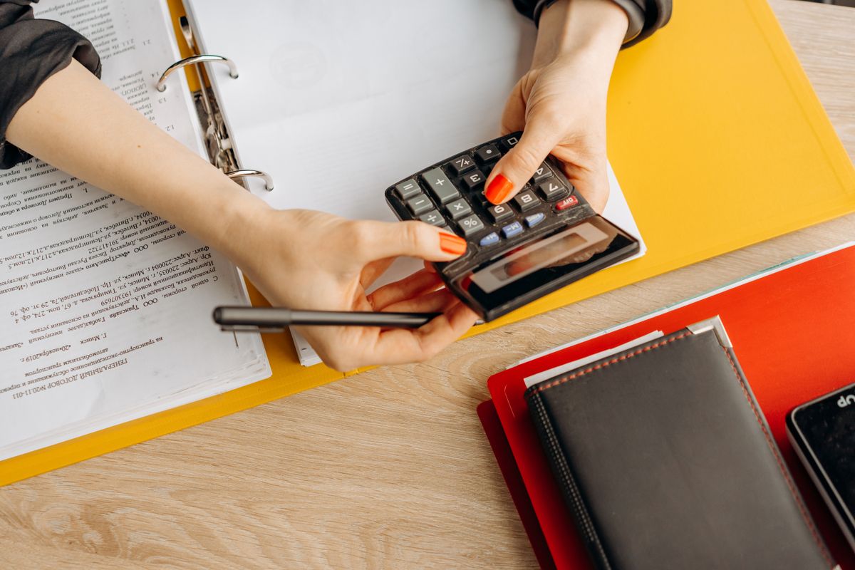Mulher fazendo cálculos financeiros com calculadora e papéis em ambiente profissional