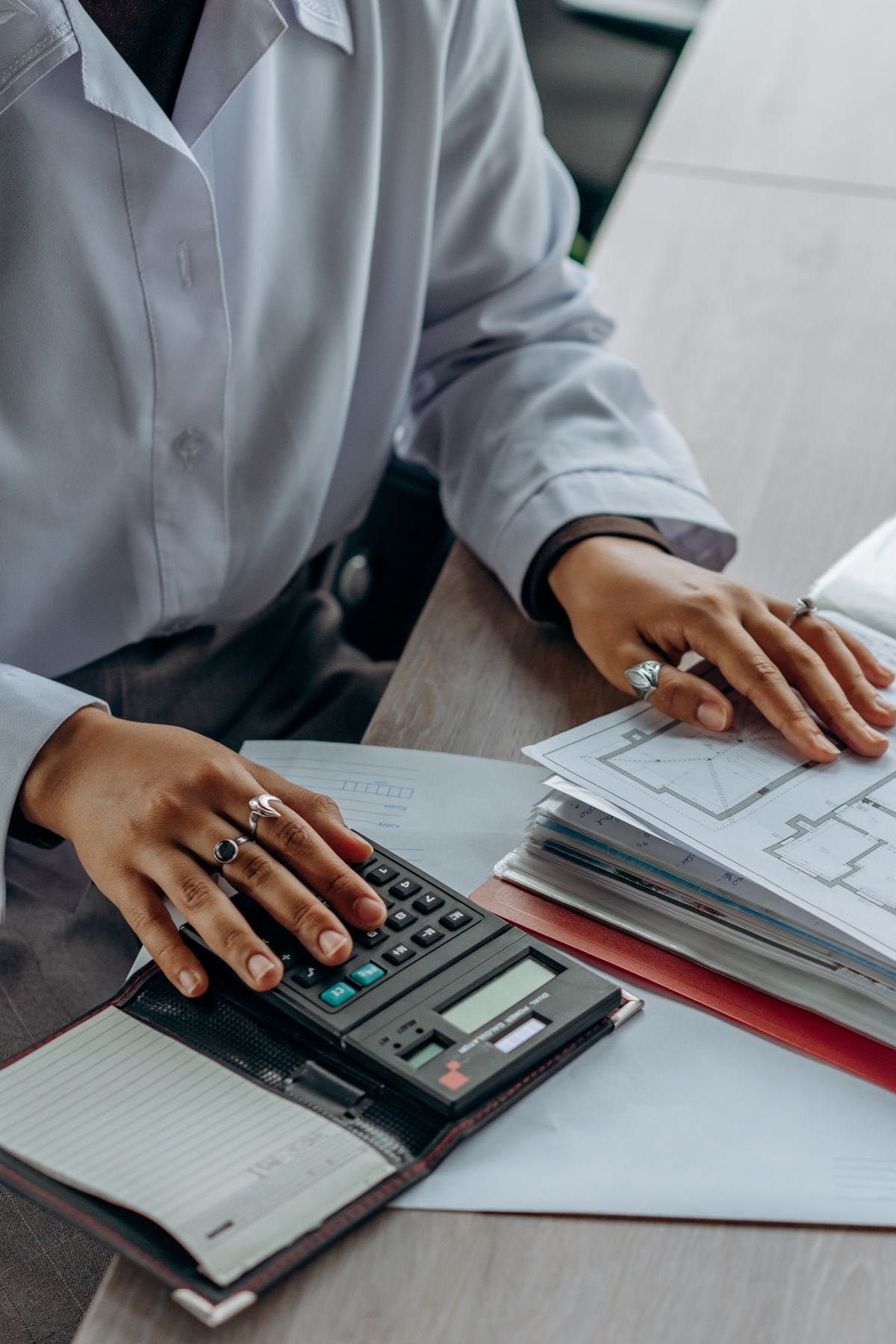 Pessoa usando calculadora e analisando documentos financeiros em escritório de contabilidade